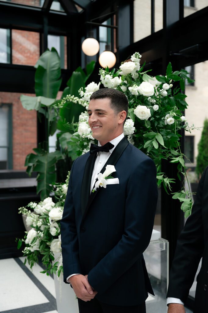 Groom smiling as he watches his bride walk down the aisle