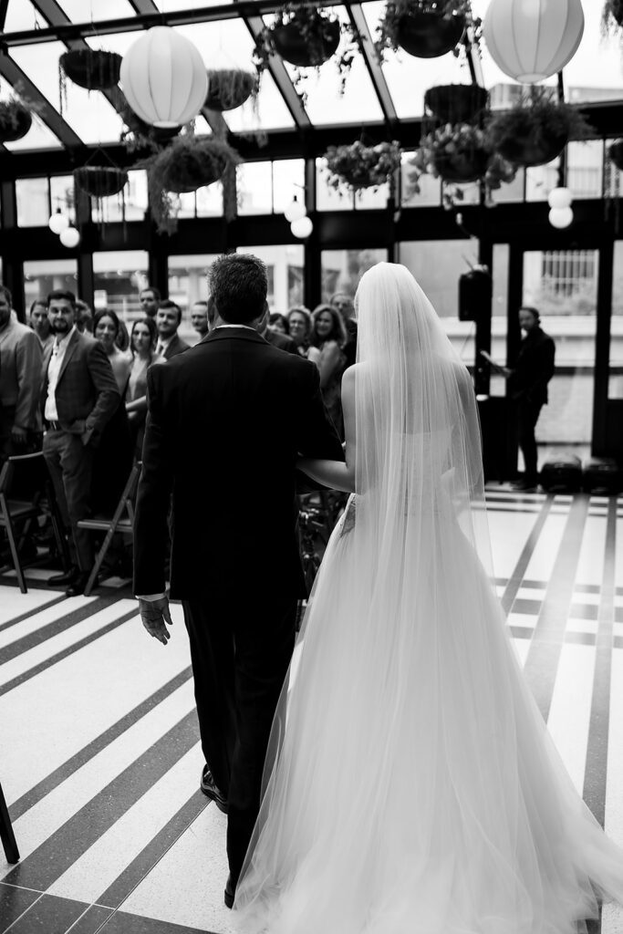 Bride walking with her father down the aisle during her Shinola Hotel wedding ceremony in The Birdy Room of the Shinola Hotel