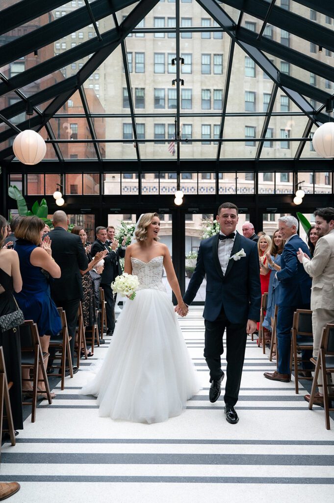 Bride and groom walking back down the aisle as husband and wife after their Shinola Hotel wedding ceremony in The Birdy Room
