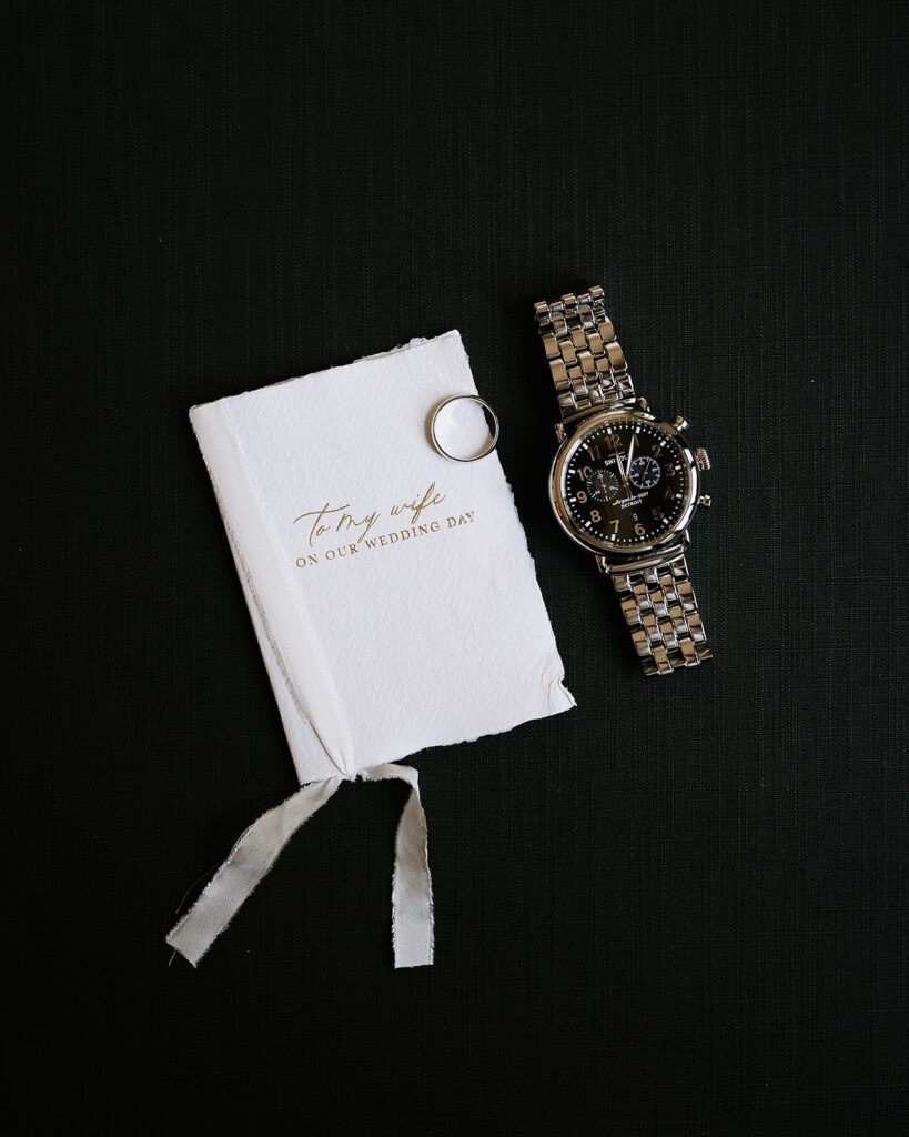 Grooms wedding detail shot with watch. ring. and vow book