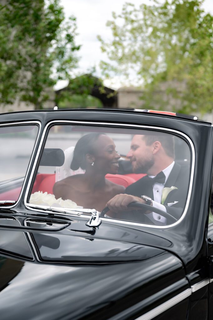 Bride and groom smiling at each other inside a 1940 Ford Deluxe convertible from Motor City Vintage Rentals