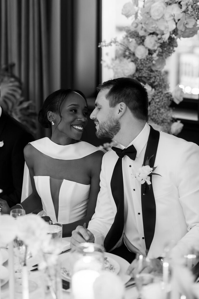Bride and groom smiling at each other during dinner