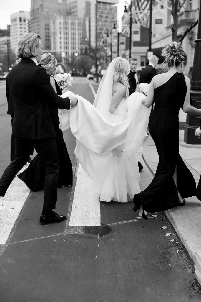 Candid wedding photo of a wedding party walking across the street