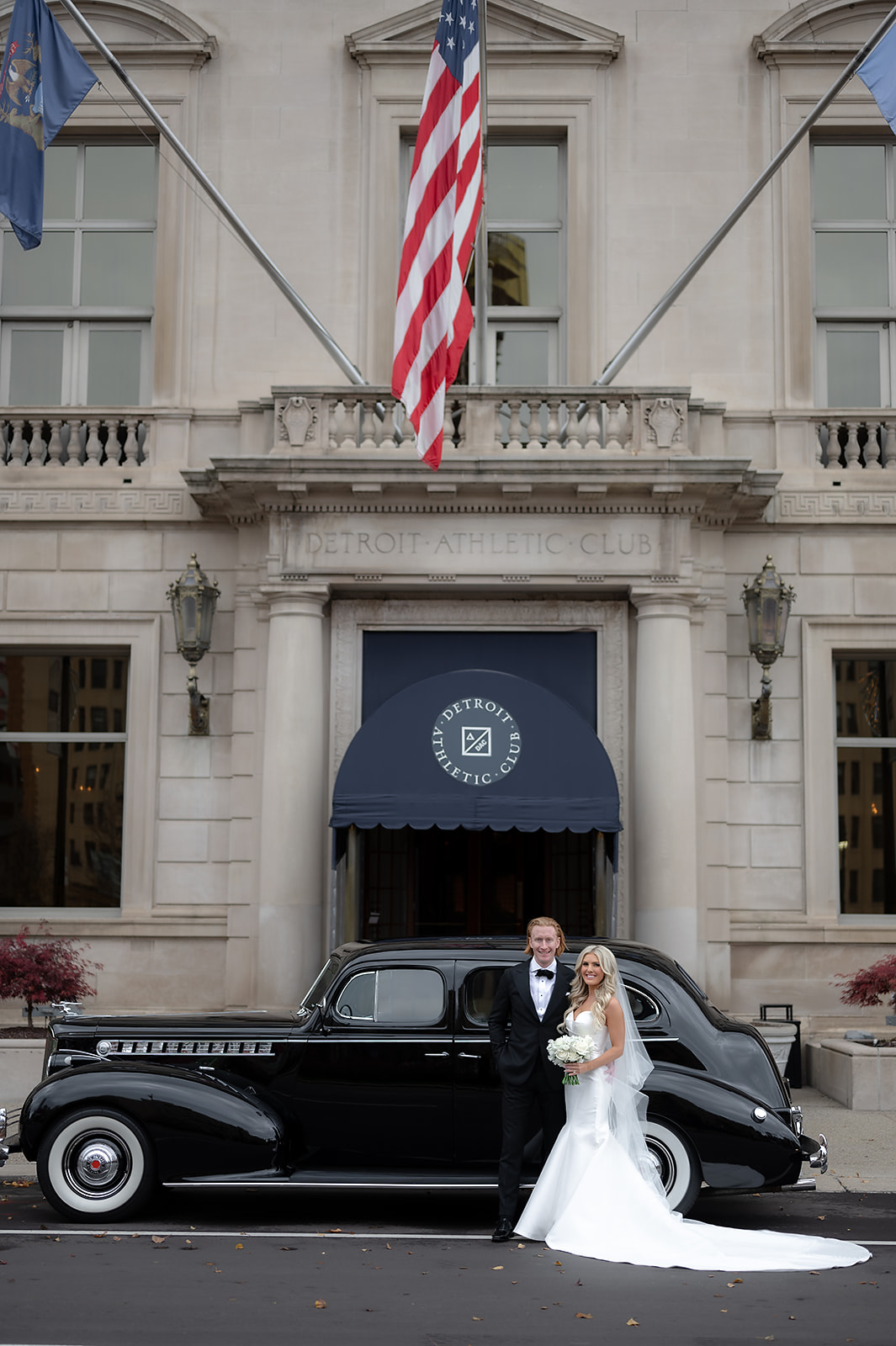Bride and groom posing outside of Detroit Athletic Club for their wedding portraits with a 1940 Detroit Packard