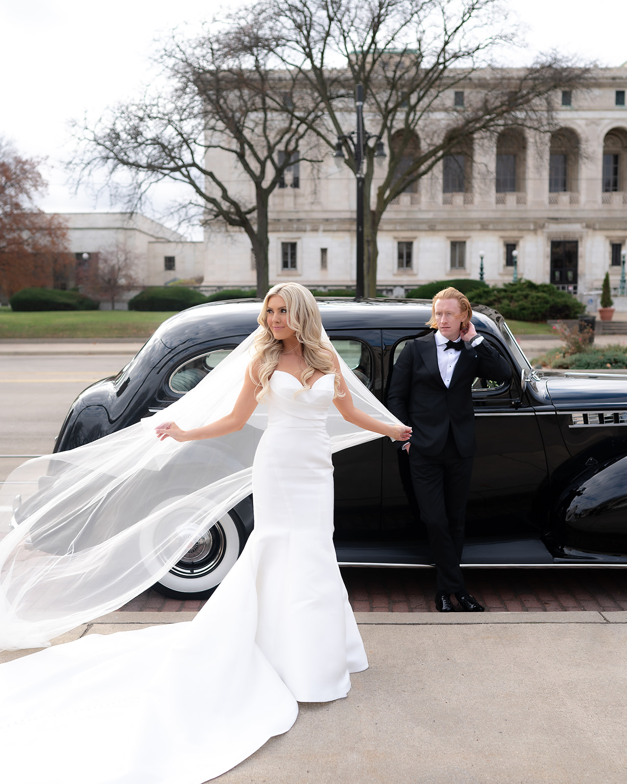Bride and groom posing in front of a vintage car for their Detroit wedding portraits outdoors