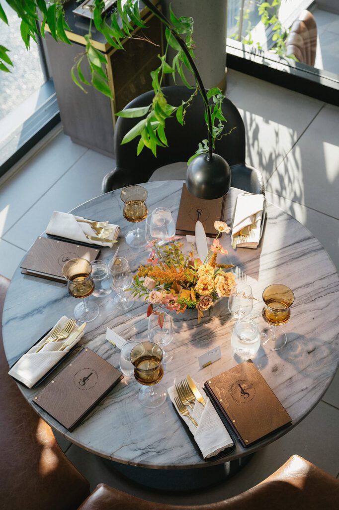 Overhead view of a round table set for guests at an MDRD Grand Plaza wedding, complete with gold flatware and a vibrant floral arrangement.