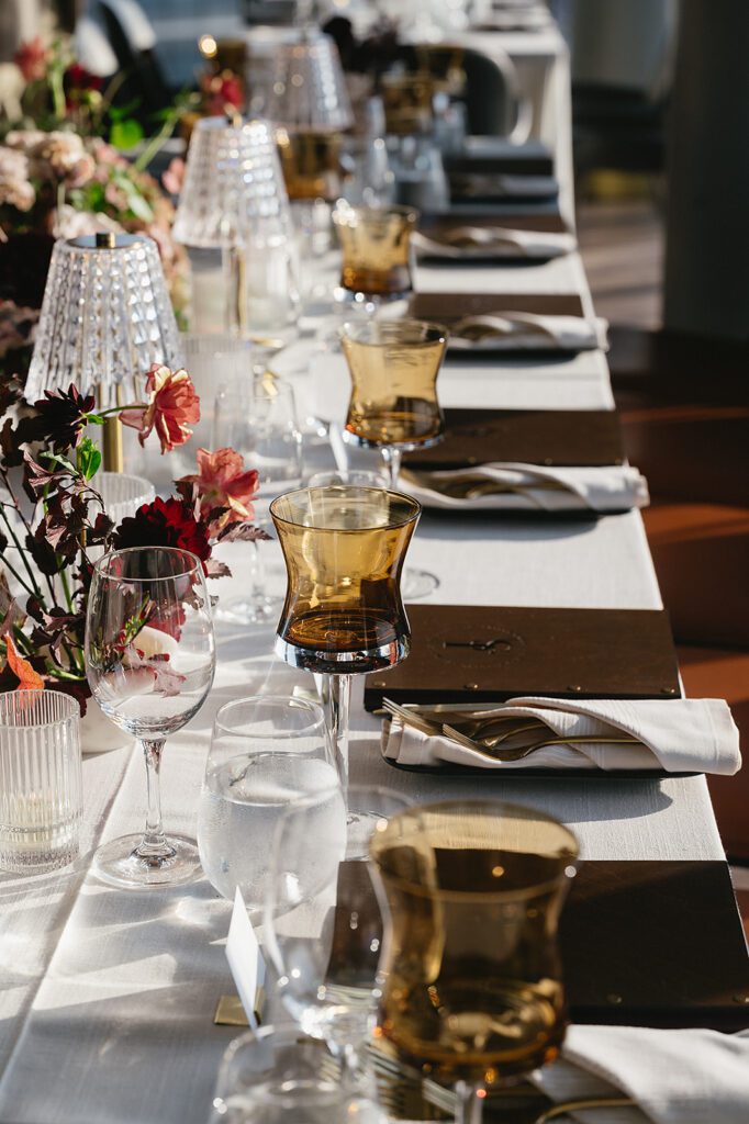 Long banquet-style reception table at an MDRD Grand Plaza wedding, decorated with crystal lamps, amber glassware, and lush florals.