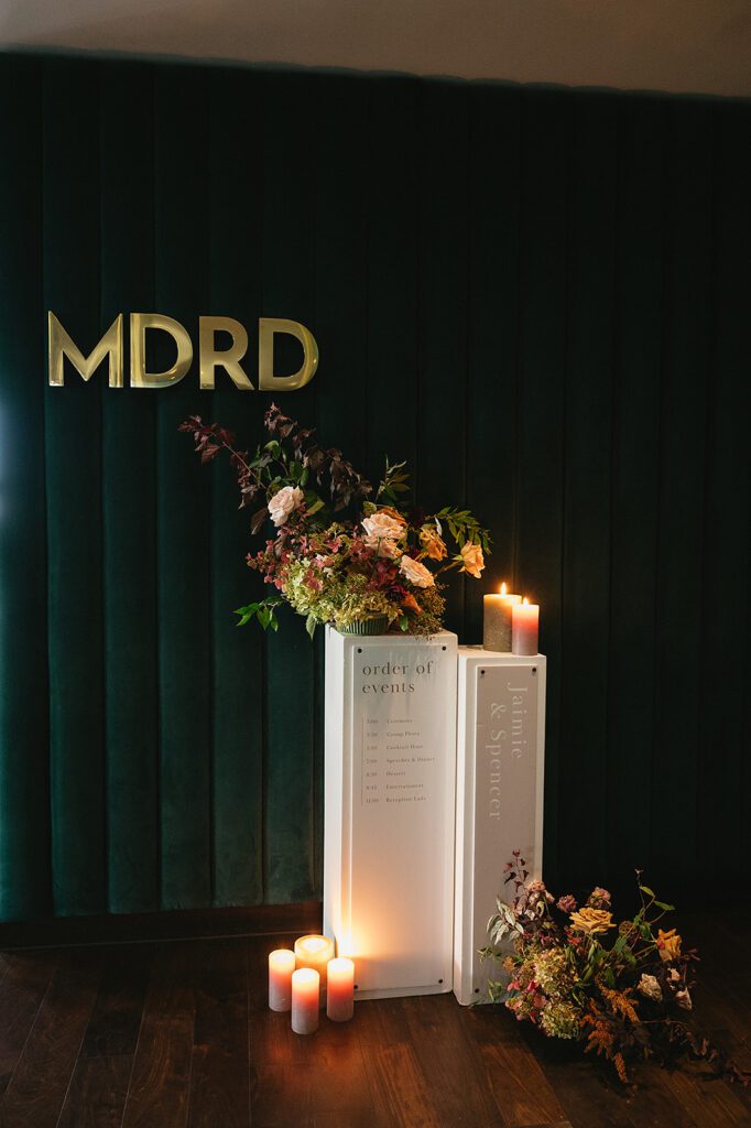 Modern signage with florals and candles welcomes guests and shares the event timeline at an MDRD Grand Plaza wedding.