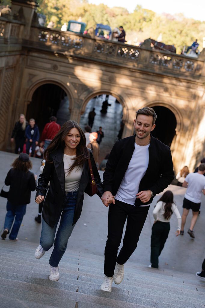 Couple running up the Bethesda Terrace steps hand-in-hand in Central Park.