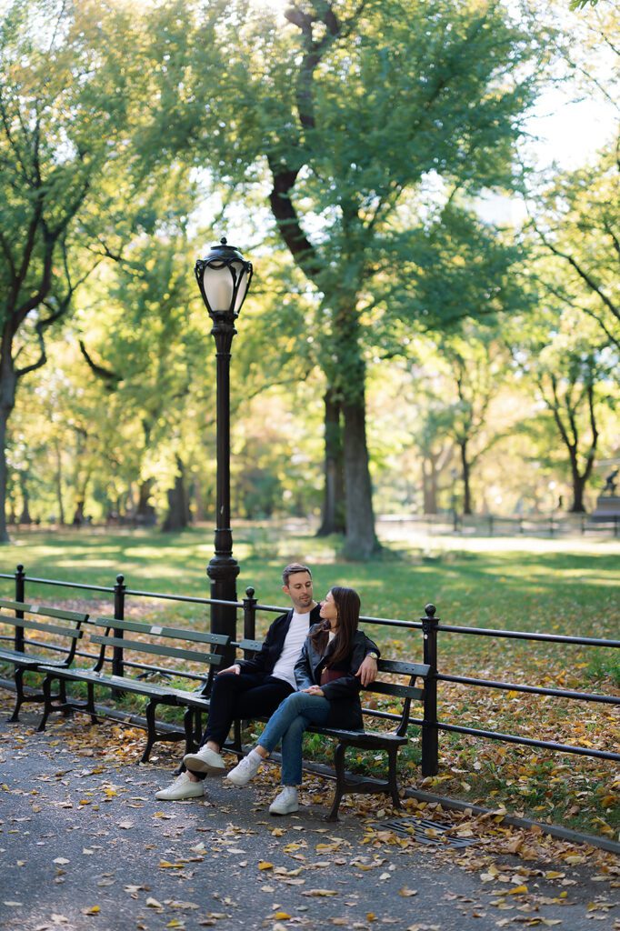 Couple sitting on a bench under a lamp post along The Mall in Central Park during fall.