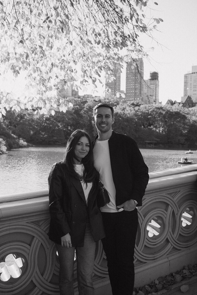 Black and white photo of a couple posing on Bow Bridge for their NYC engagement photos in Central Park