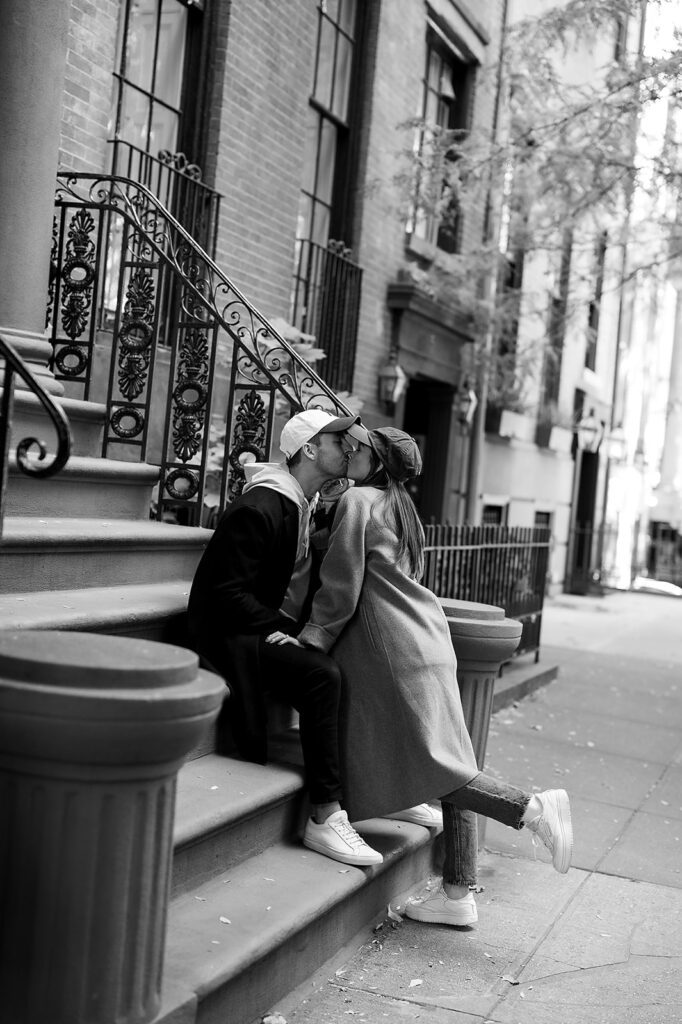 Black and white photo of a couple sharing a kiss on the steps of a brownstone in Greenwich Village during their NYC engagement photos.