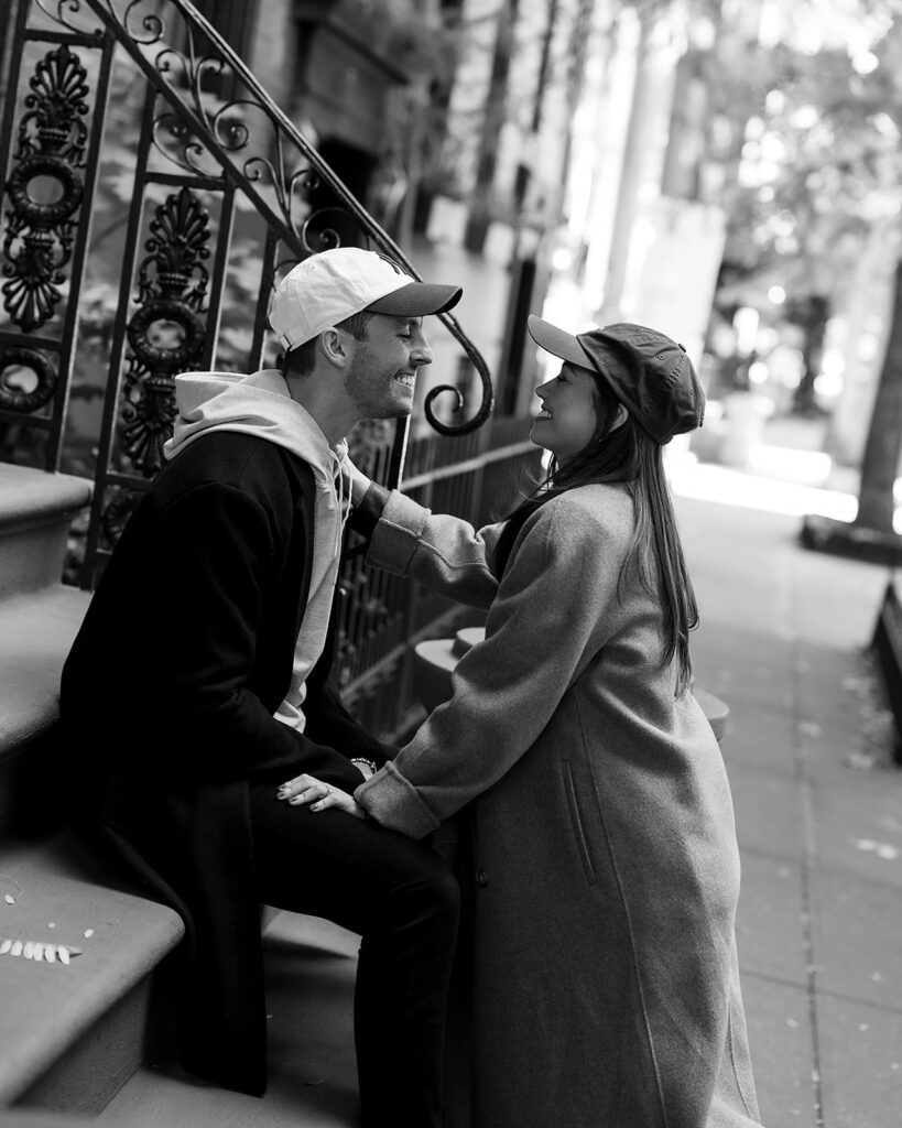 Black and white photo of a couple smiling and leaning toward each other on brownstone steps in Greenwich Village.