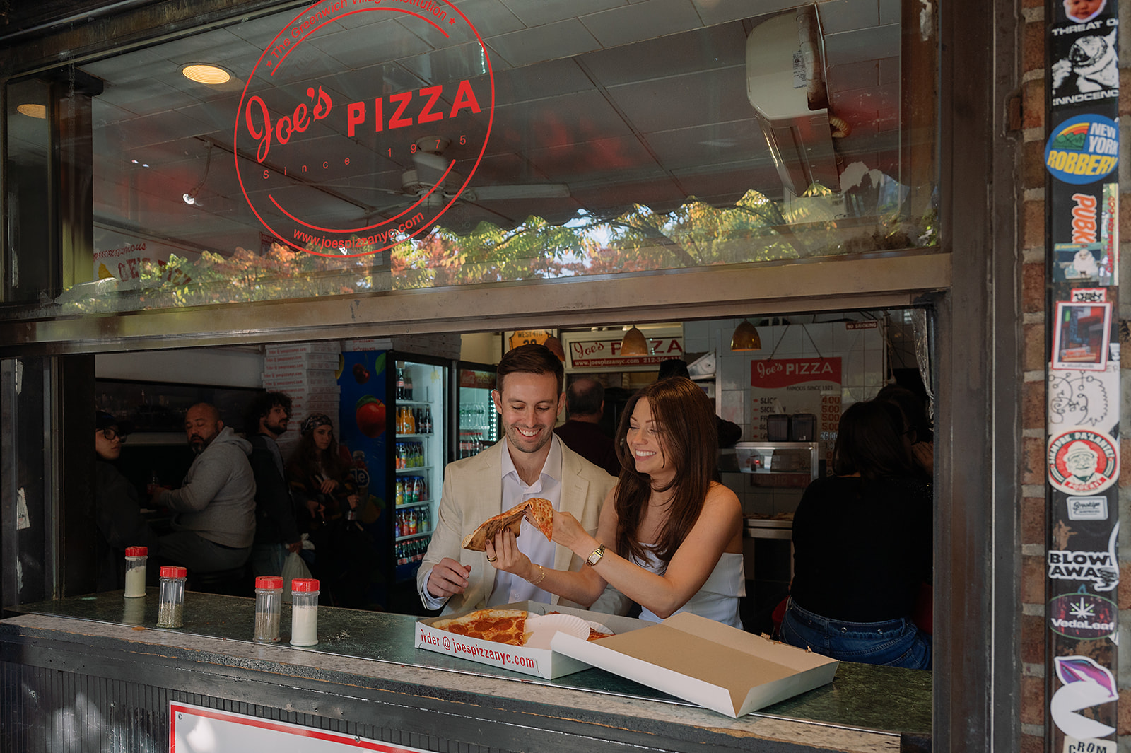 Couple sharing a slice of pizza at Joe’s Pizza window during NYC engagement photos in Greenwich Village.