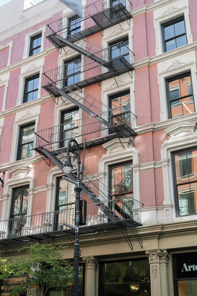 Pink SoHo building with black fire escapes and street lamp in NYC.
