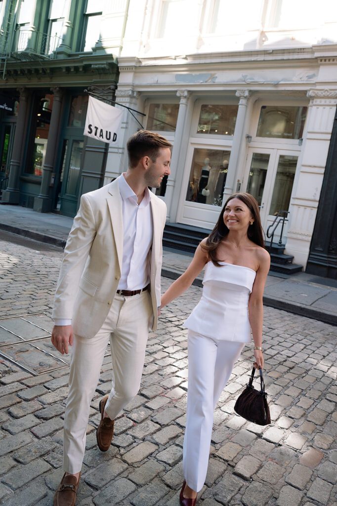 Couple walking hand in hand across cobblestone street in SoHo, NYC.