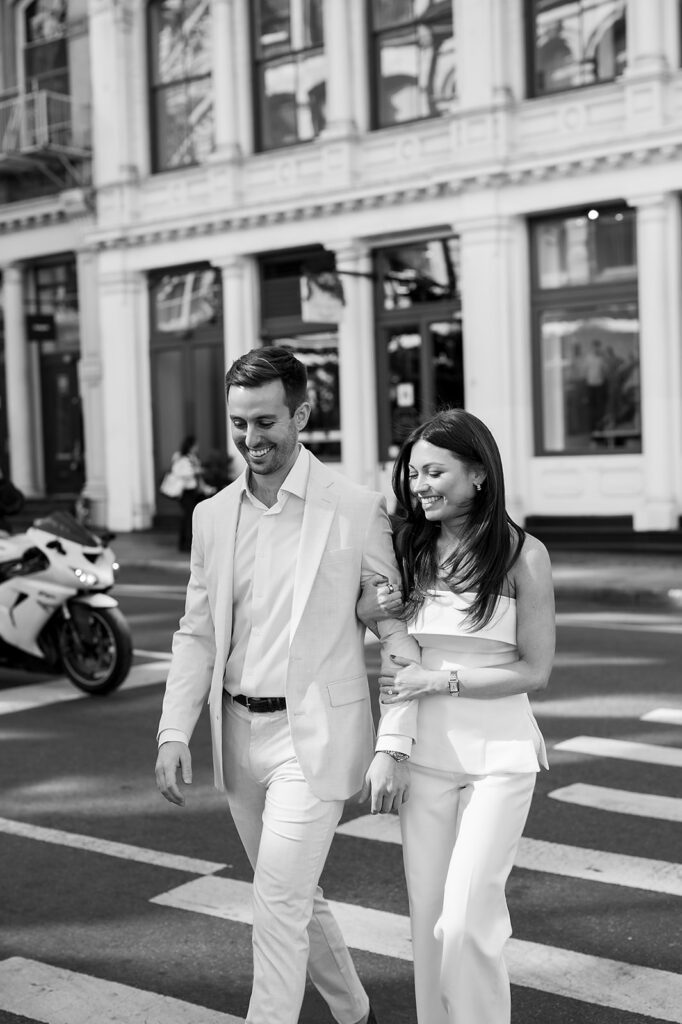 Black and white photo of couple walking arm in arm across a crosswalk in SoHo.