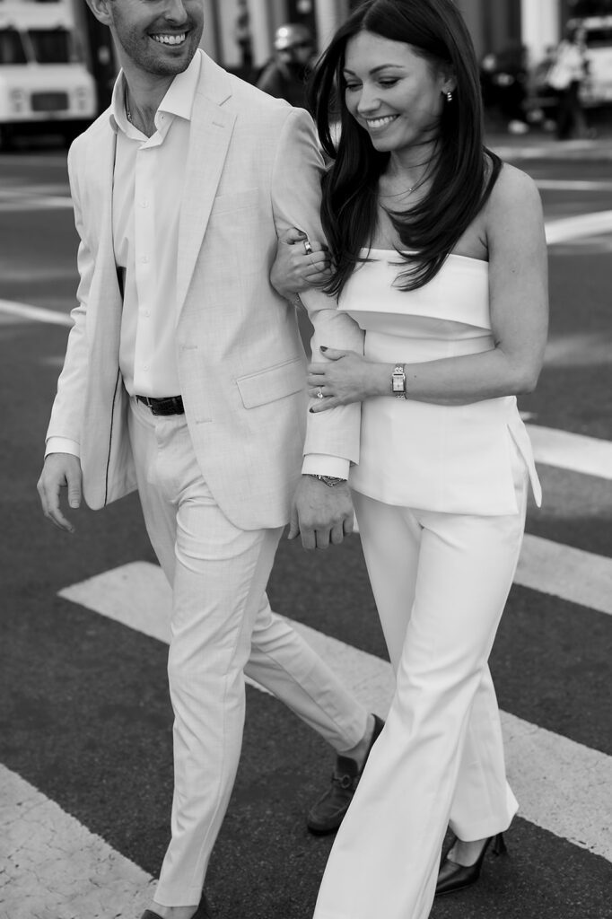 Black and white photo of couple walking arm in arm across a crosswalk in SoHo.