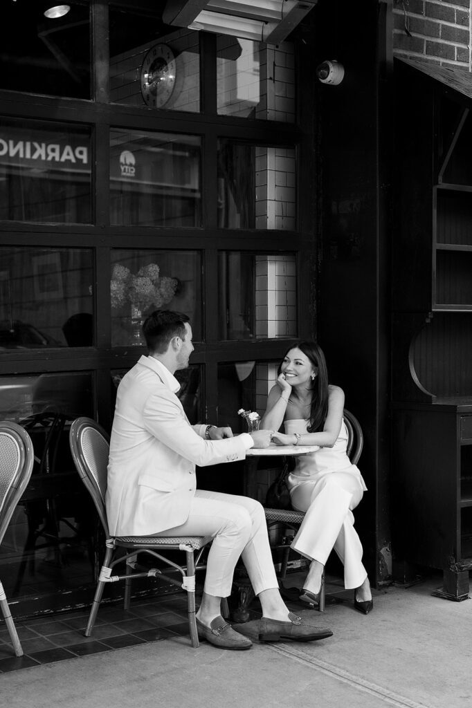 Couple smiling together while sitting outside at a café in SoHo during their engagement photos.