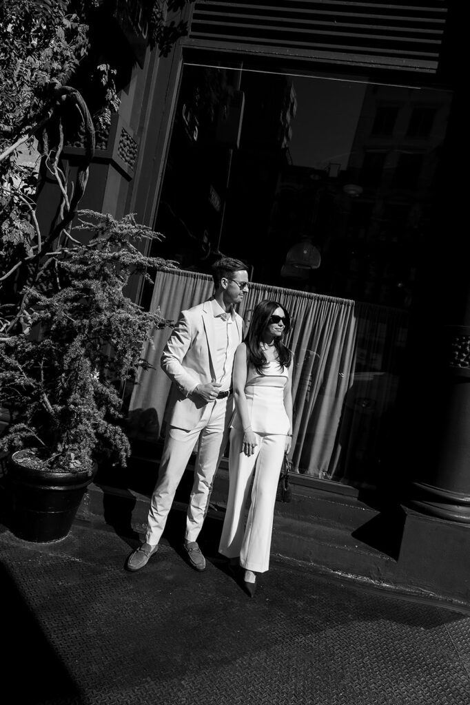 Black and white photo of couple wearing sunglasses, standing confidently outside a SoHo building.