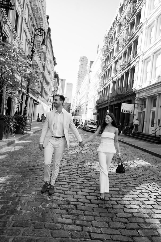 Couple walking hand in hand across cobblestone street in SoHo, NYC.