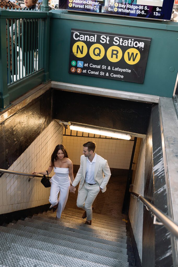 Couple walking up the Canal Street subway stairs holding hands during NYC engagement photos.