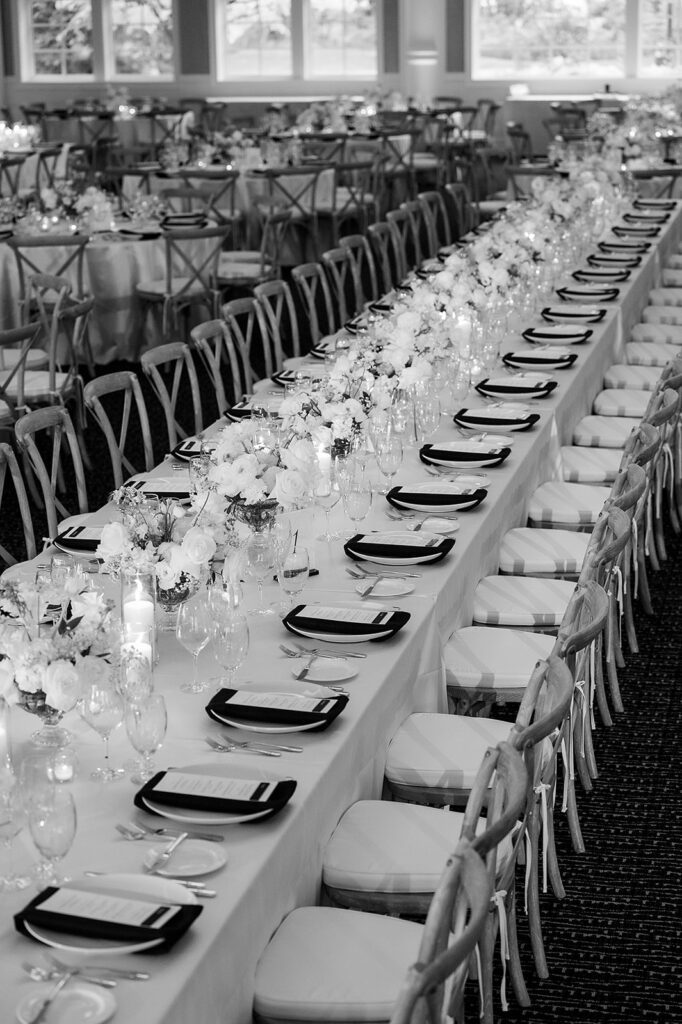 Black and white photo of a wedding reception place setting with a printed dinner menu, black napkin, and candlelight at Bay Harbor Yacht Club.