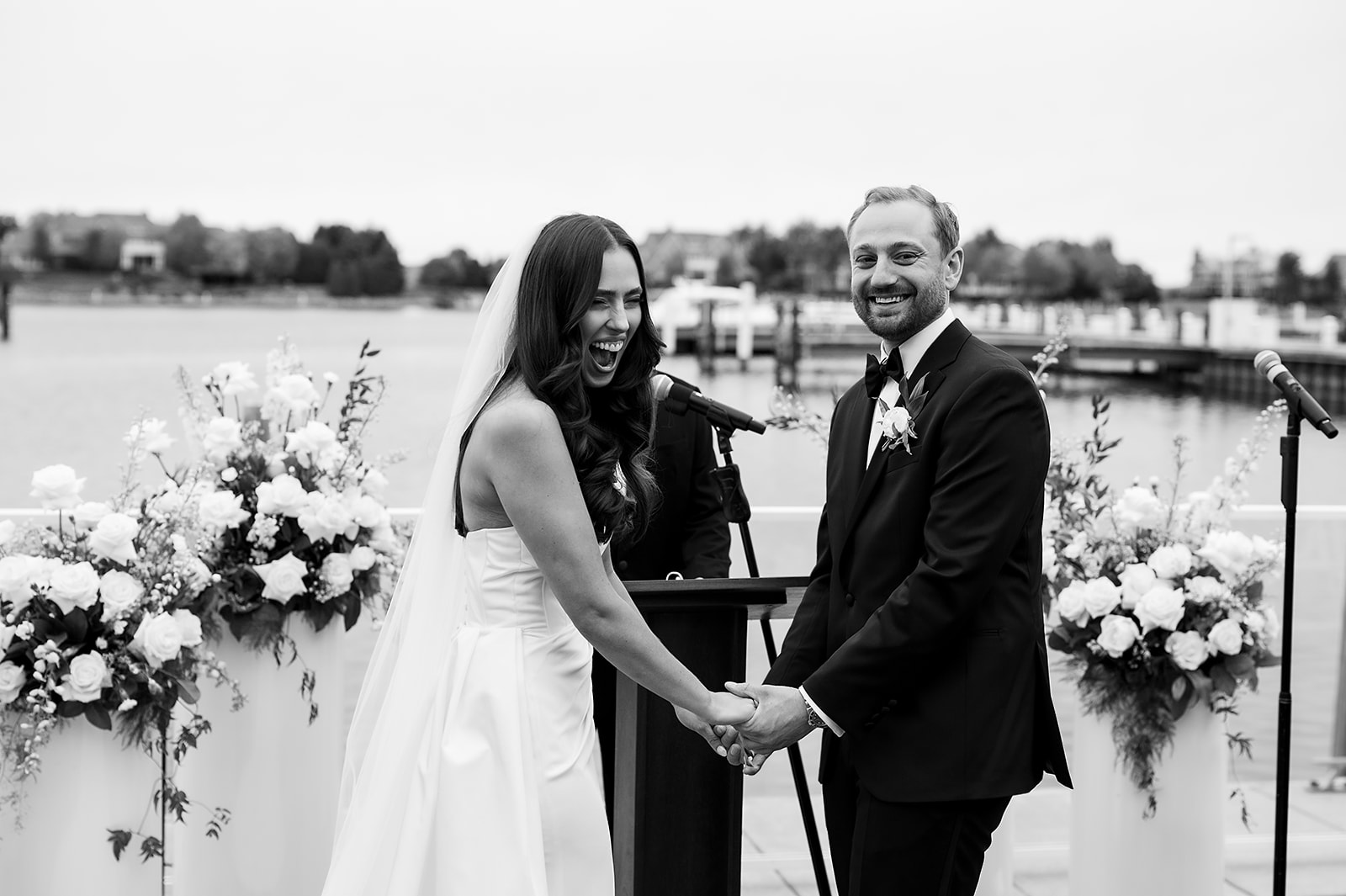 Bride and groom holding hands and smiling at the altar with white floral arrangements in the background.