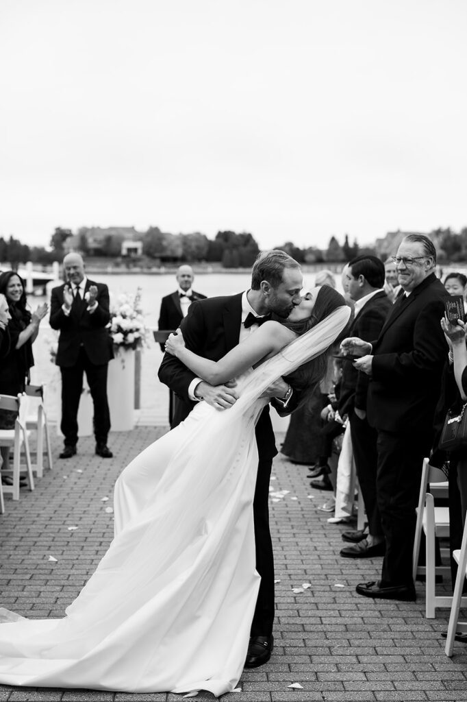 Black and white photo of a bride and grooms end of aisle dip kiss during their Bay Harbor Yacht Club Promenade Dock wedding ceremony