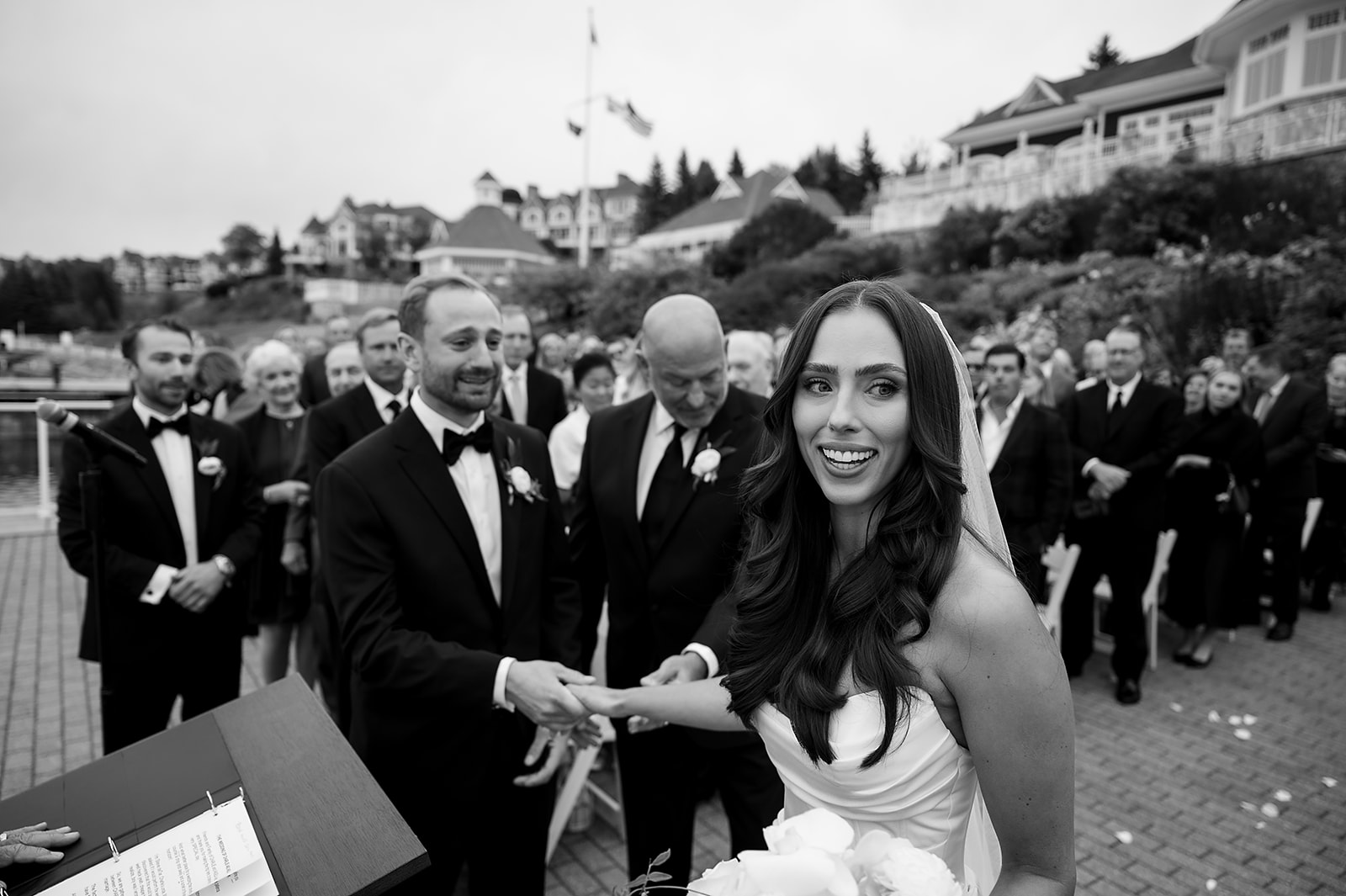 Black and white photo of a bride grabbing her husbands hand as her father hands her off during the ceremony