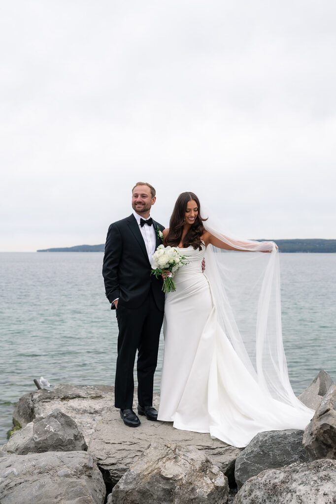 Bride and groom posing on a rock with Little Traverse Bay in the background