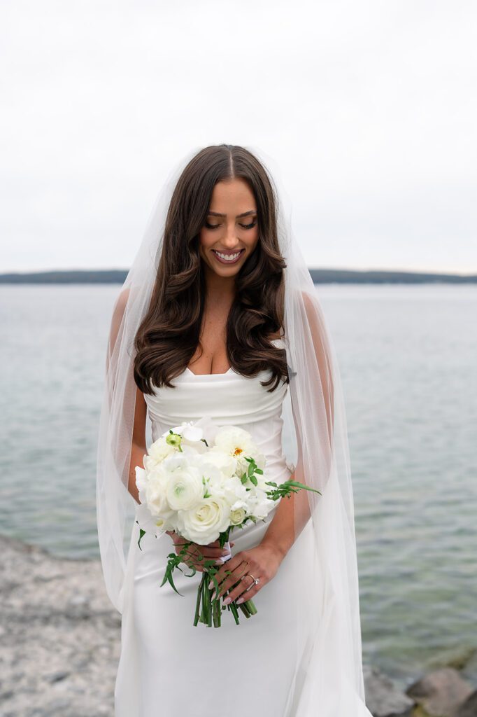 Bride posing in front of Little Traverse Bay while holding her classic white bouquet by Sweetwater Floral