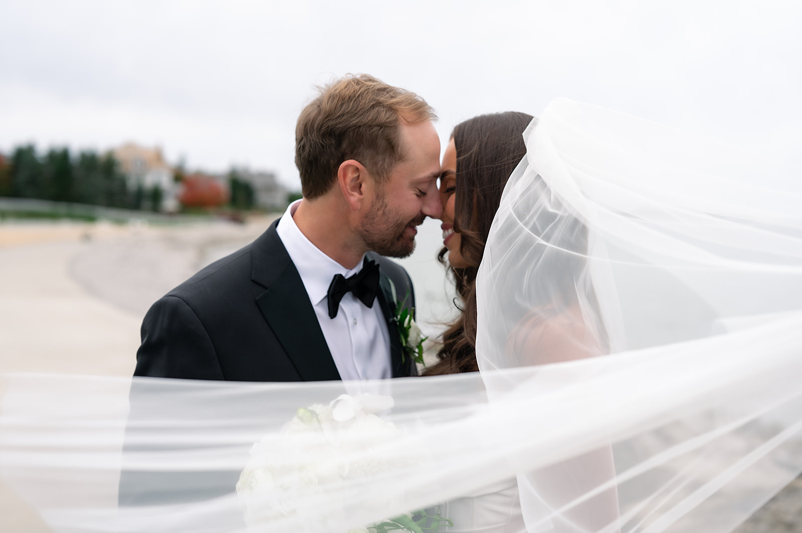 Bride and groom posing along the shoreline of Little Traverse Bay during portraits.