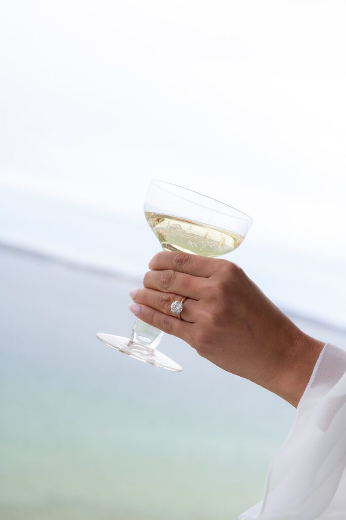 Bride holding a glass of champagne showing her engagement ring with the bay in the background.
