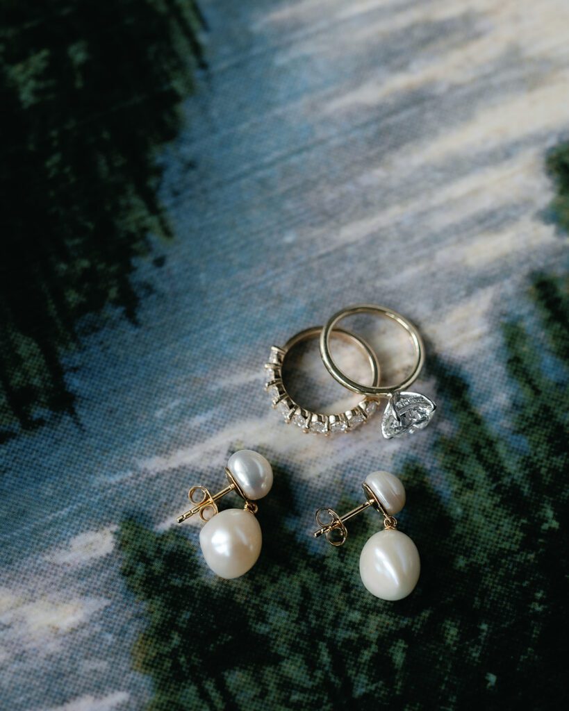 Pearl earrings and gold wedding rings arranged on soft blue fabric during morning preparations.