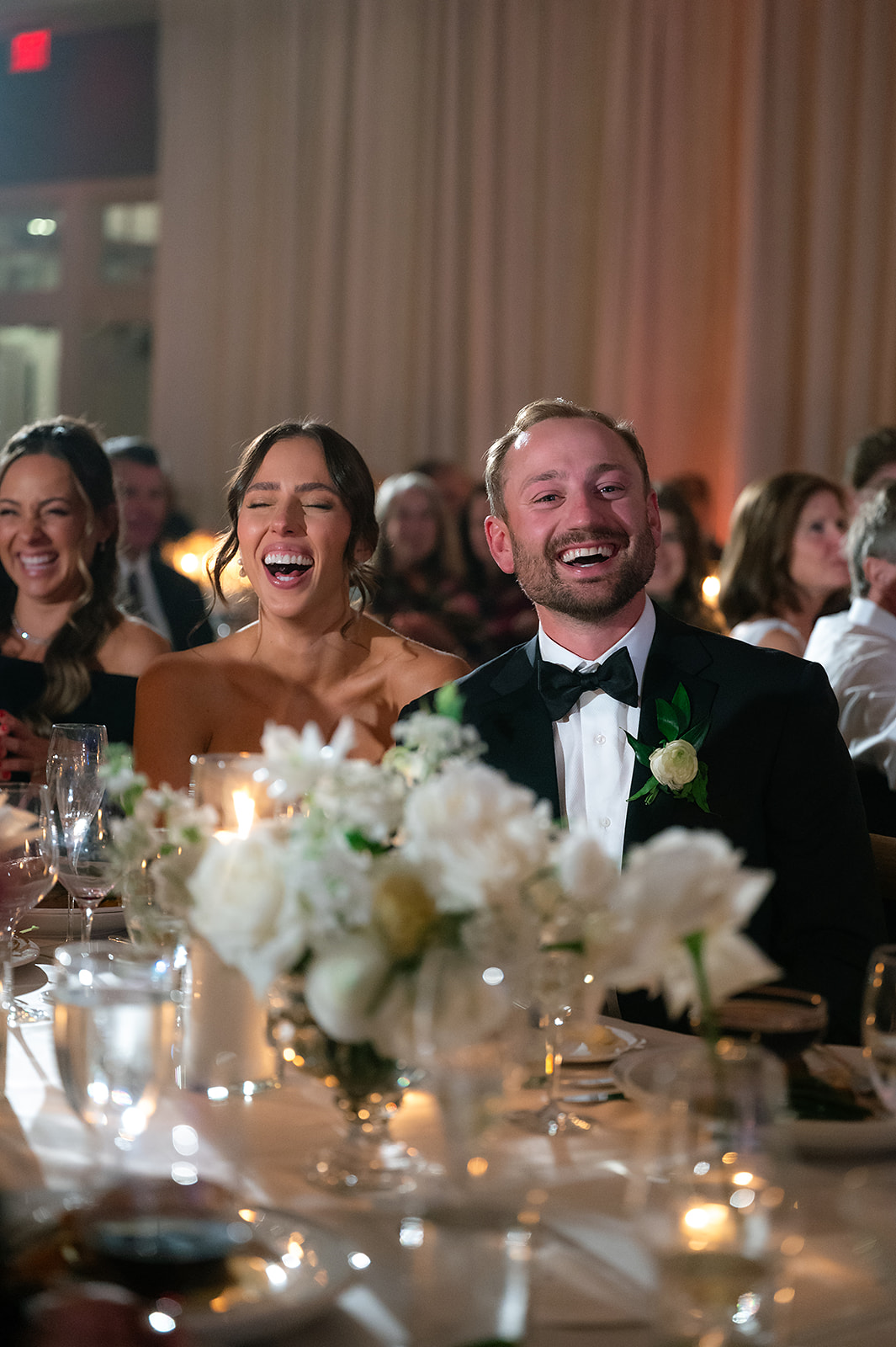 Bride and groom laughing together during wedding toasts inside the Lange Center Ballroom at Bay Harbor Yacht Club.