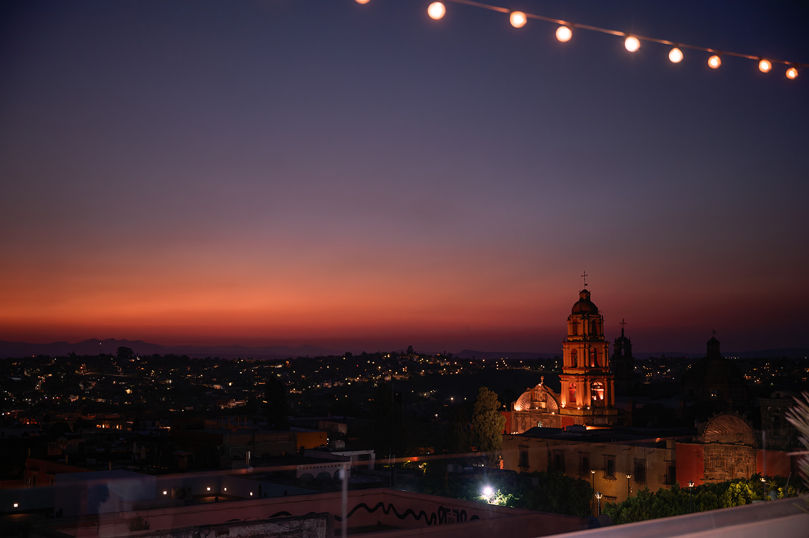 Rooftop view of Bekeb bar in San Miguel de Allende at golden hour with guests enjoying cocktails and city views.