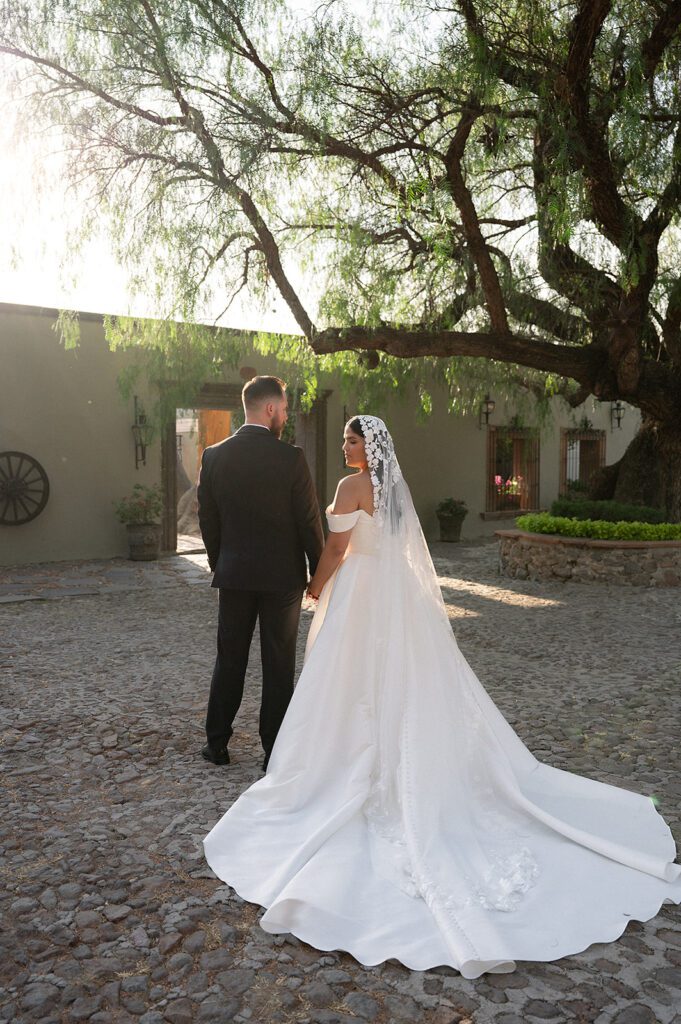 Bride and groom holding hands in courtyard with long wedding dress train at Hacienda San Luis Gonzaga