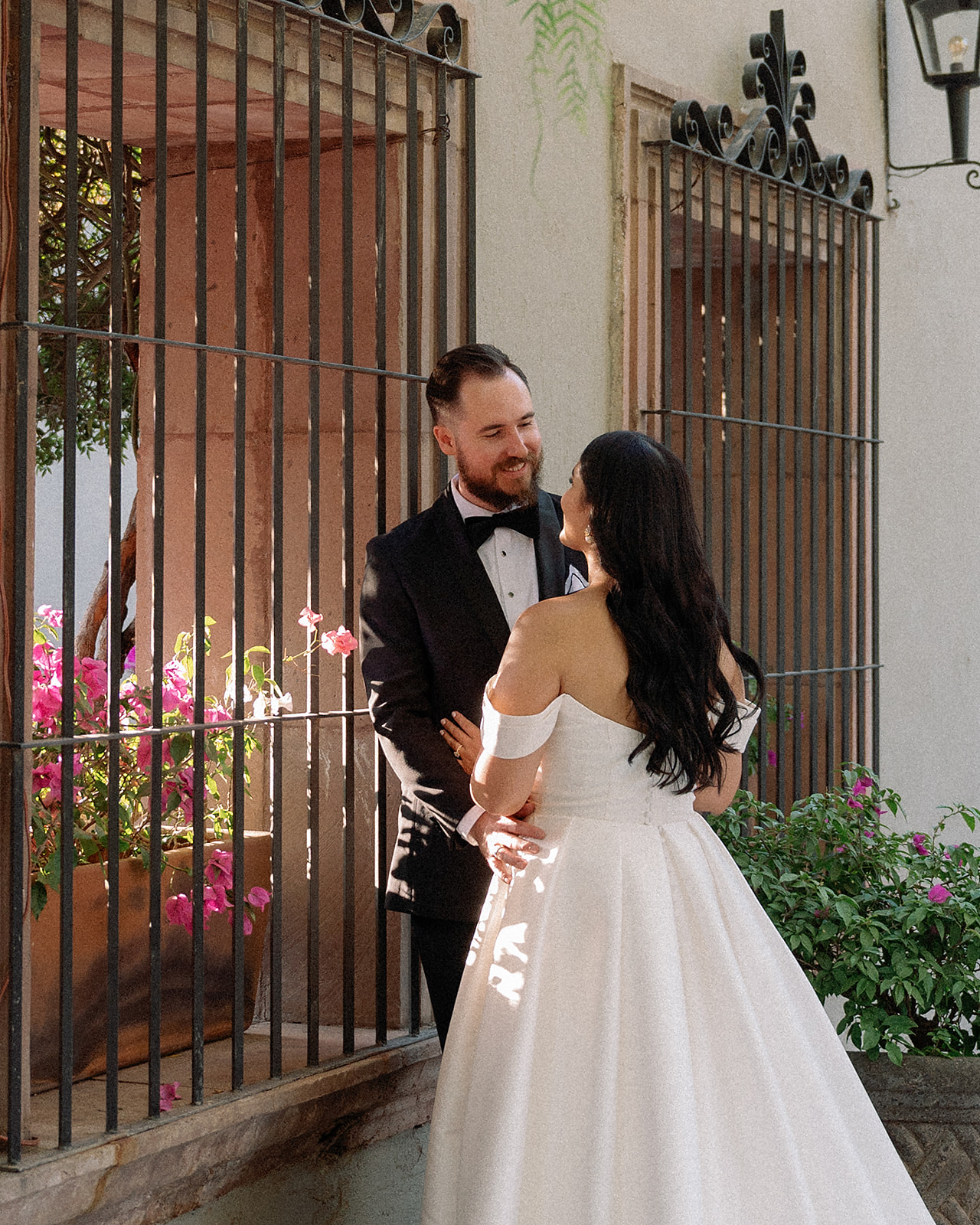 Bride and groom sharing a quiet moment beside a gate with pink flowers at San Miguel de Allende venue