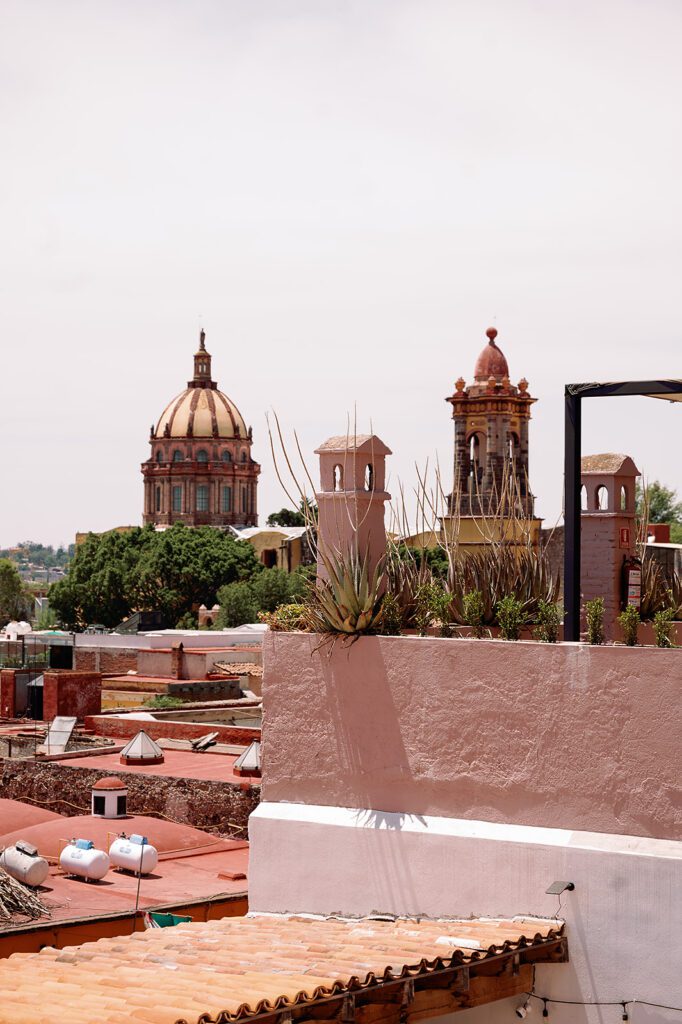 View of San Miguel de Allende rooftops and cathedral domes under the midday sun.