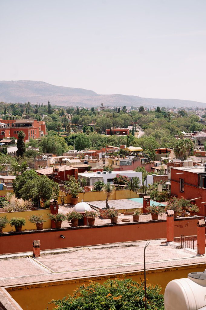 Colorful view of San Miguel de Allende from a rooftop terrace, surrounded by lush greenery and terracotta buildings.