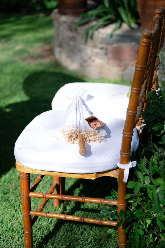 White parasol and rose petals placed on a wooden ceremony chair