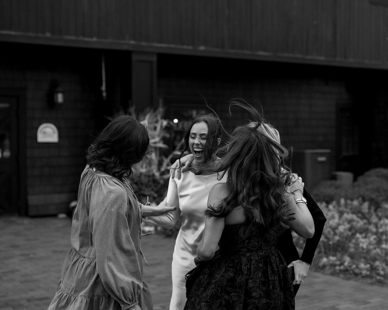 Candid black-and-white moment of the bride laughing and embracing friends outside the Northern Michigan venue.