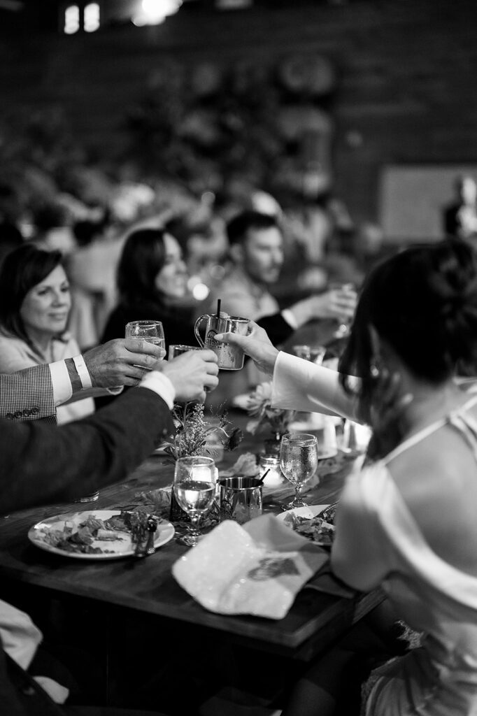 Black-and-white photo of guests raising drinks in a celebratory toast during a Northern Michigan wedding weekend.