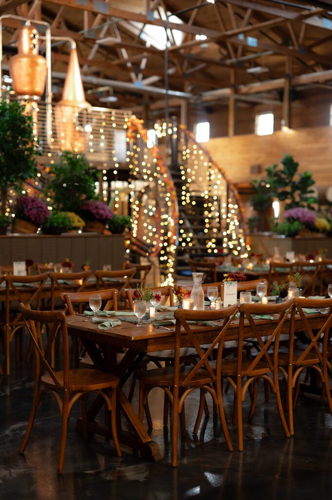 Rustic indoor setting with wooden tables, greenery, and string lights creating a cozy atmosphere for the Northern Michigan wedding welcome party.