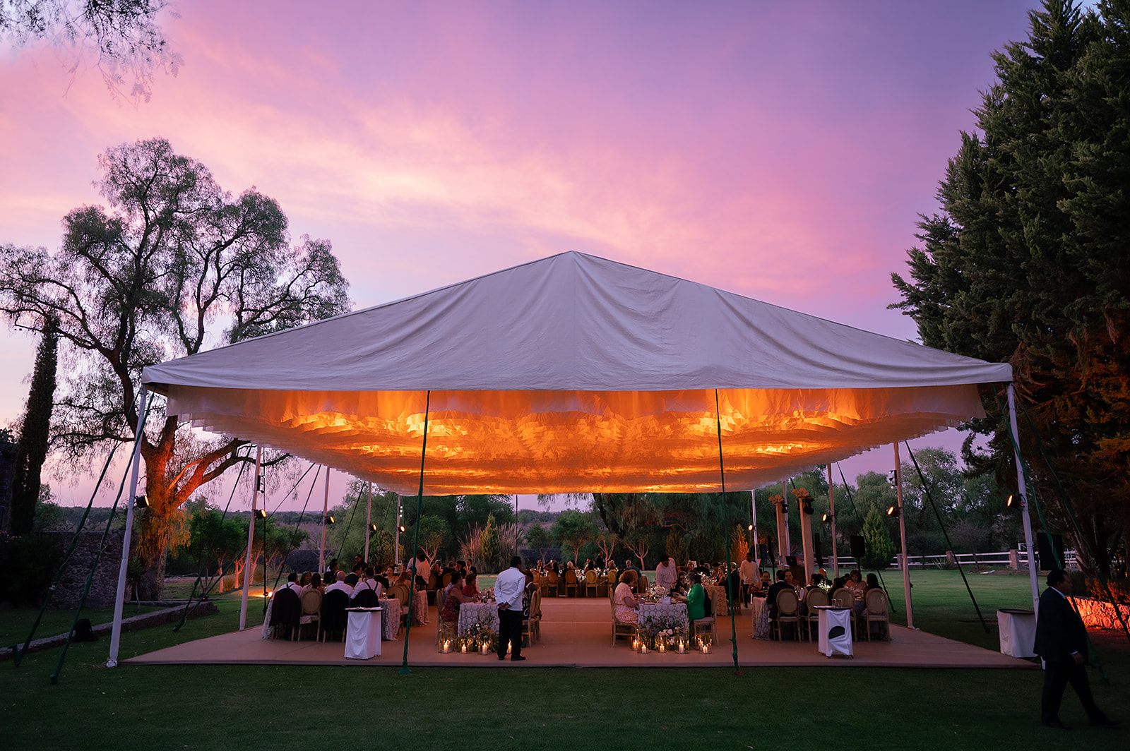 Tented wedding reception at Hacienda San Luis Gonzaga glowing at sunset with warm lighting and guests seated beneath the canopy.