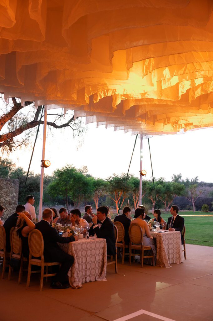 Tented wedding reception at Hacienda San Luis Gonzaga glowing at sunset with warm lighting and guests seated beneath the canopy.