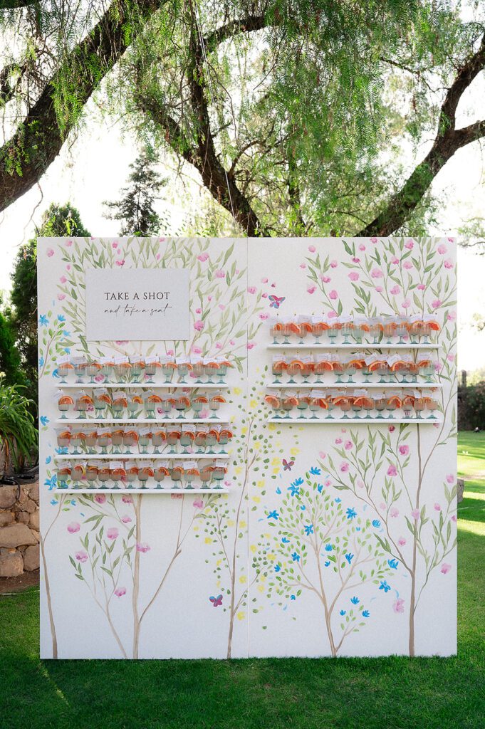 Wide view of custom “Take a Shot and Take a Seat” escort wall setup at Hacienda San Luis Gonzaga wedding reception in San Miguel de Allende.