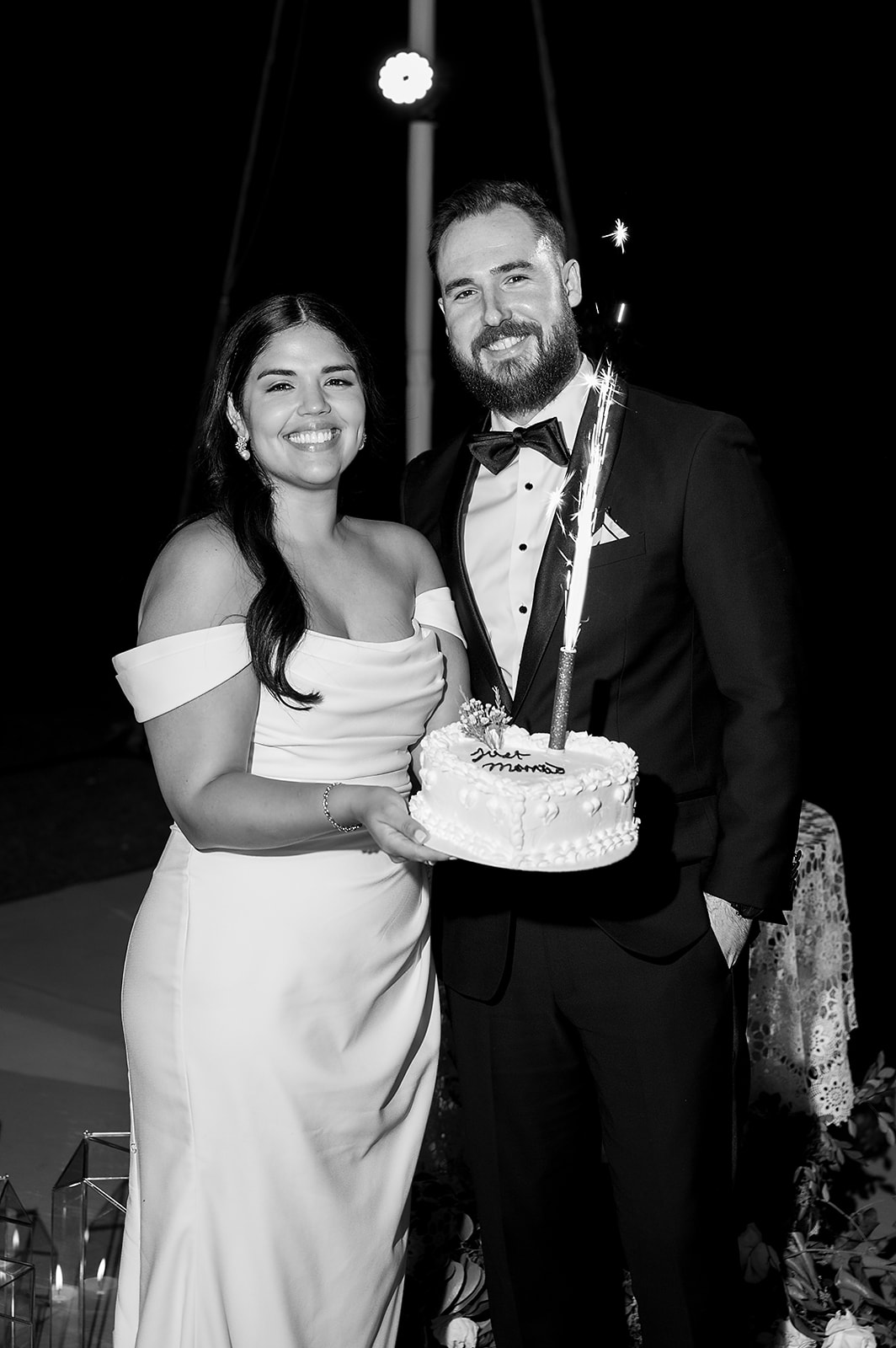 Black and white photo of a bride and groom posing with their cake