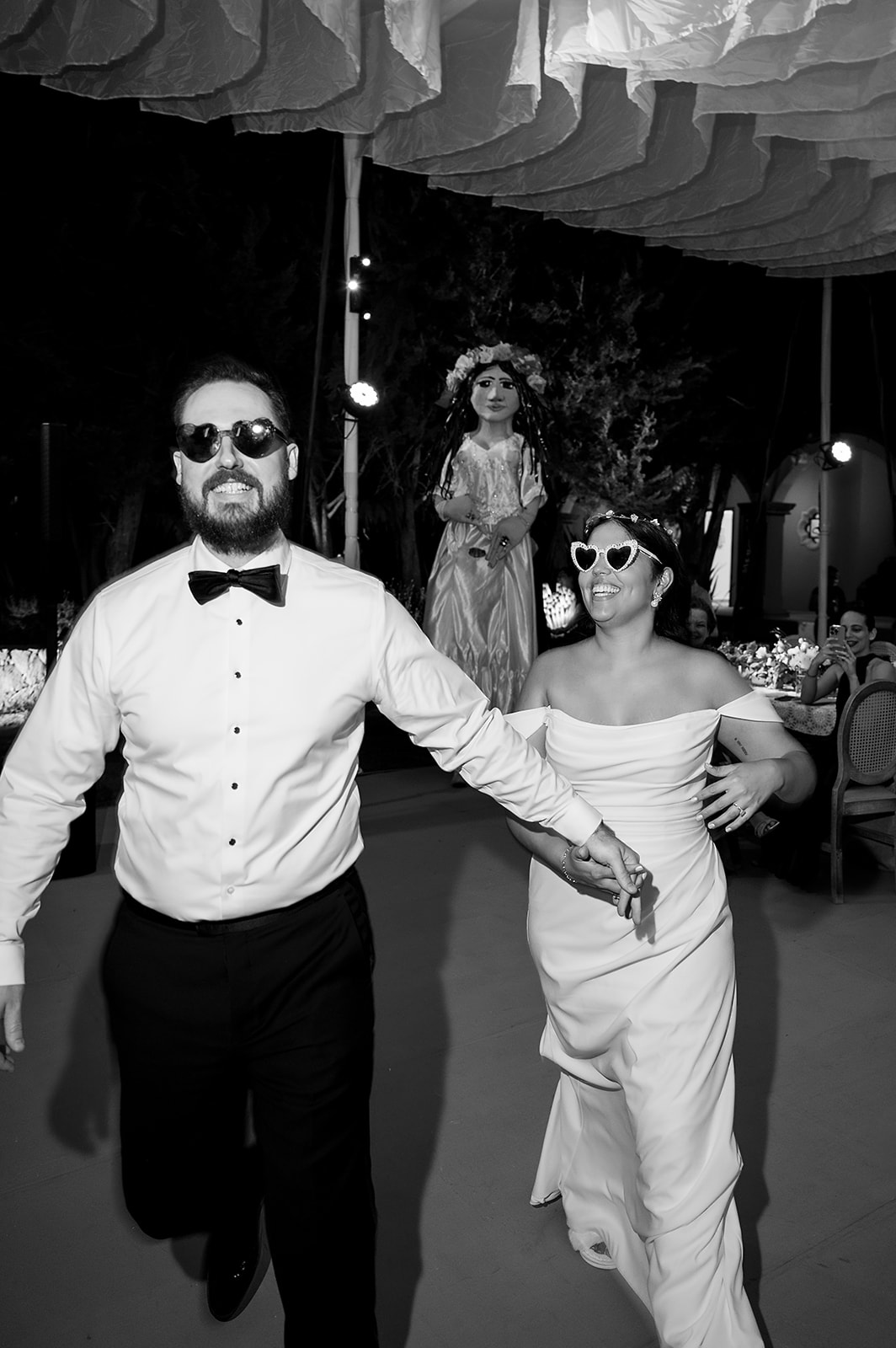 Bride and groom running hand-in-hand with smiles and heart-shaped sunglasses during wedding reception at Hacienda San Luis Gonzaga.